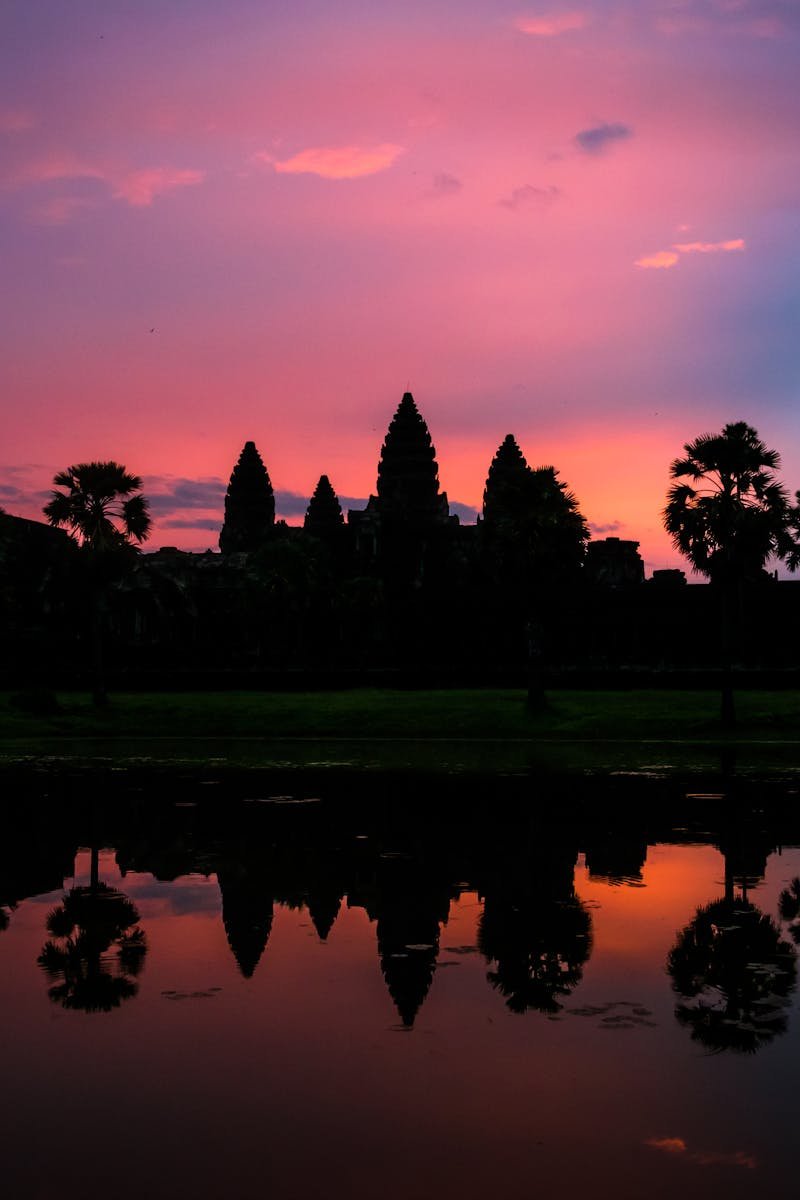 Stunning silhouette of Angkor Wat with a vibrant sunset reflecting in the surrounding water.