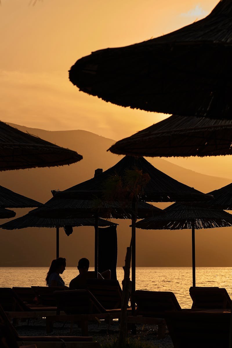 Couple enjoying a sunset at Vlorë Beach, Albania, under beach umbrellas. Perfect vacation moment.