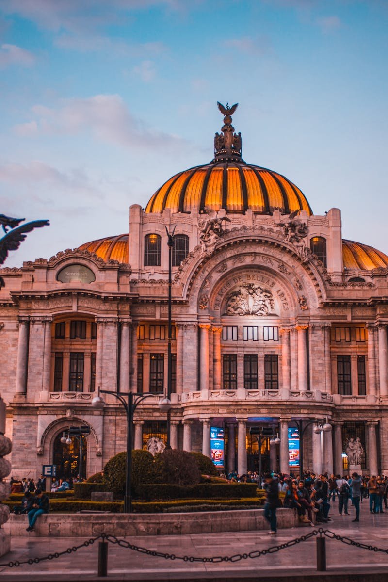 Vibrant sunset at the historic Palacio de Bellas Artes in Mexico City, bustling with tourists.