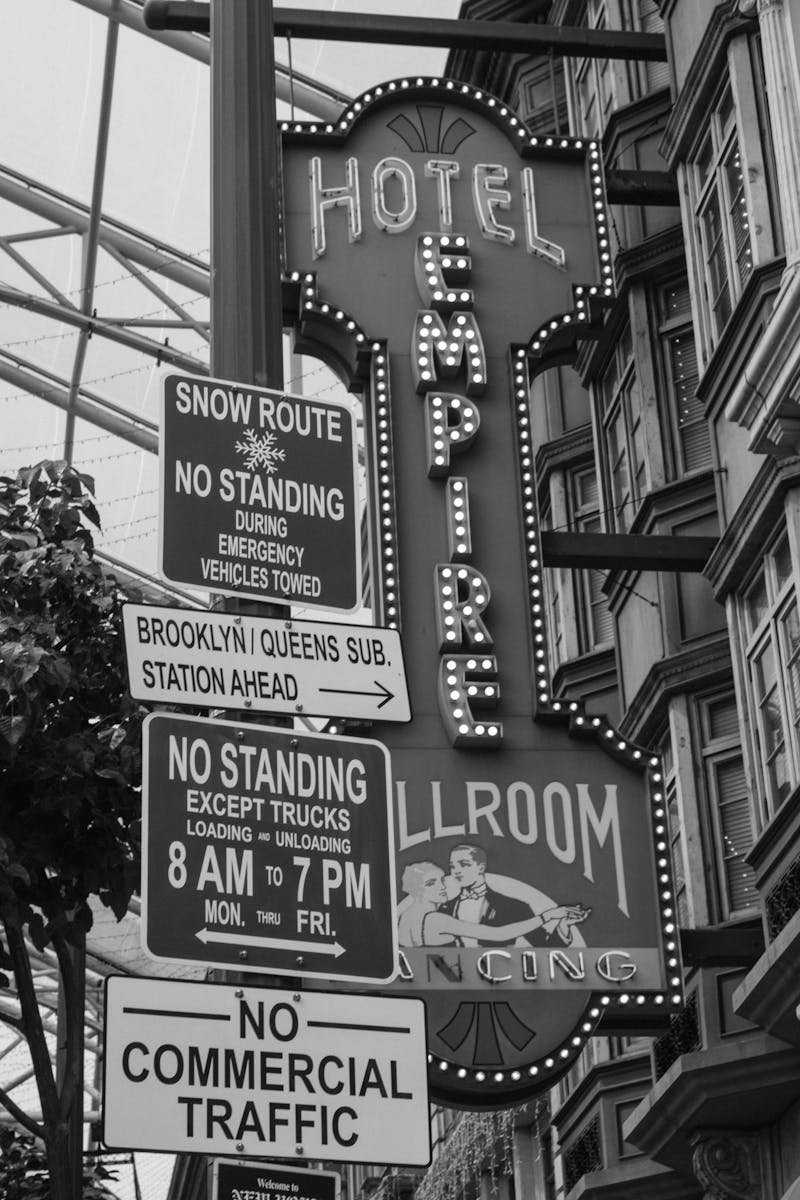 Black and white photo of Hotel Empire sign with various street signs in an urban setting.