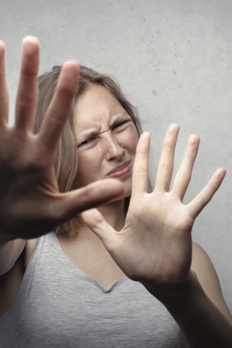 Portrait of a fearful woman in a gray tank top with hands pushed forward against a gray background.