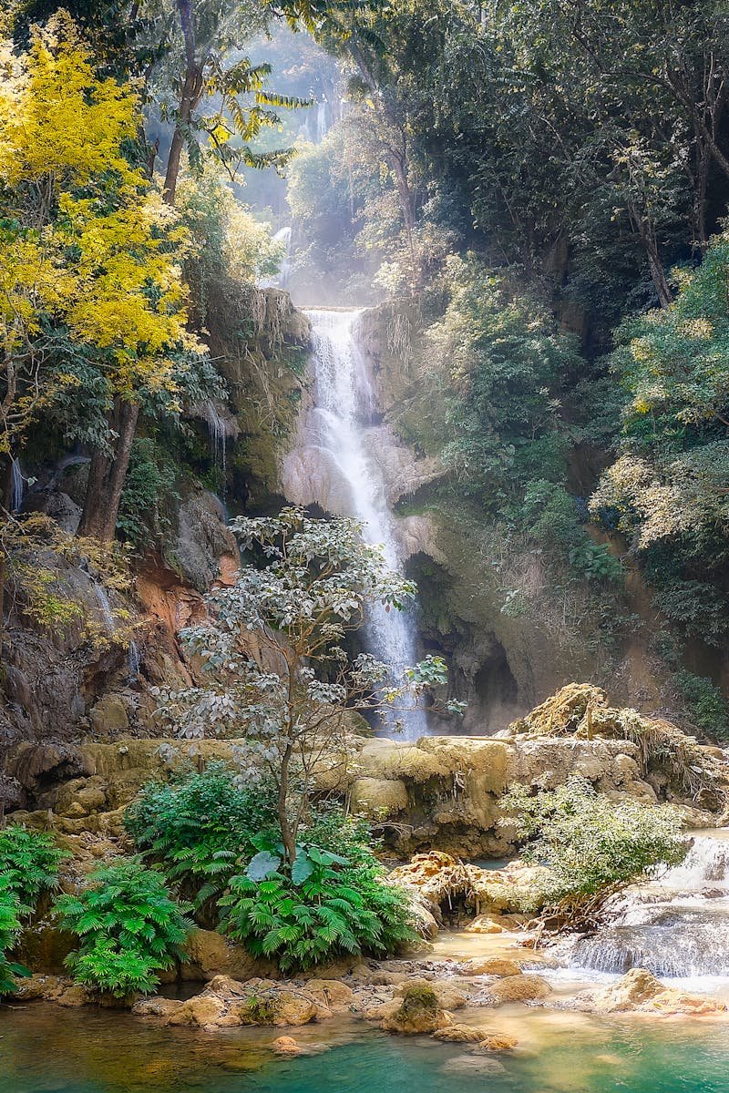 Serene waterfall cascading through dense jungle in Laos, surrounded by vibrant foliage.