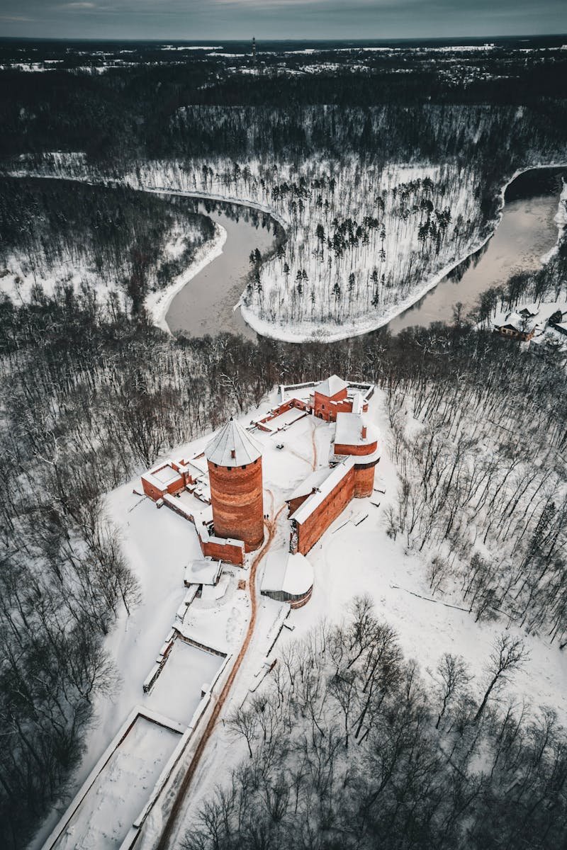 A stunning aerial view of Turaida Castle surrounded by snowy forests in Latvia during winter.