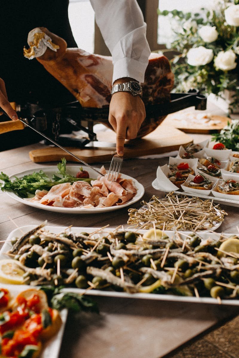 A chef slices meat in a beautifully arranged catering setup with diverse appetizing dishes.