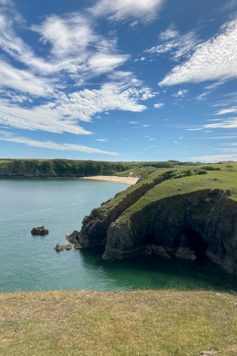 Beautiful coastal landscape featuring cliffs, green meadows, and calm sea under a bright sky.