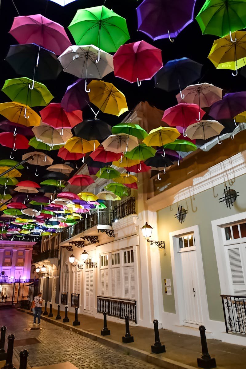 A stunning display of colorful umbrellas hanging over Calle La Fortaleza in Old San Juan, Puerto Rico, illuminated at night.