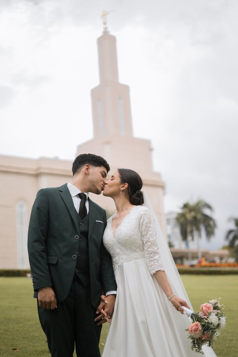 Bride and groom share a kiss at Santo Domingo LDS Temple in a lush green setting.