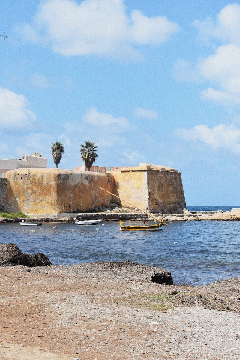 Scenic view of an ancient fort by the sea with a boat and palm trees.