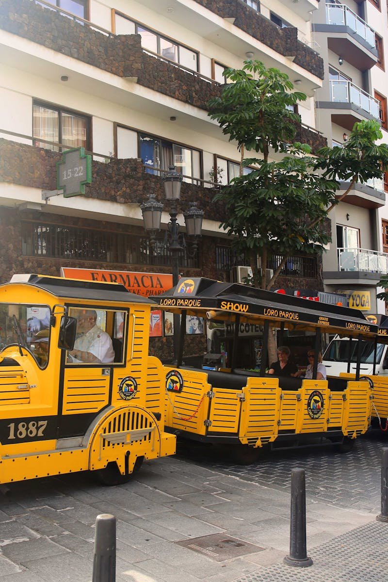 Vibrant yellow tourist train passing by urban architectural buildings in Santa Cruz de Tenerife.