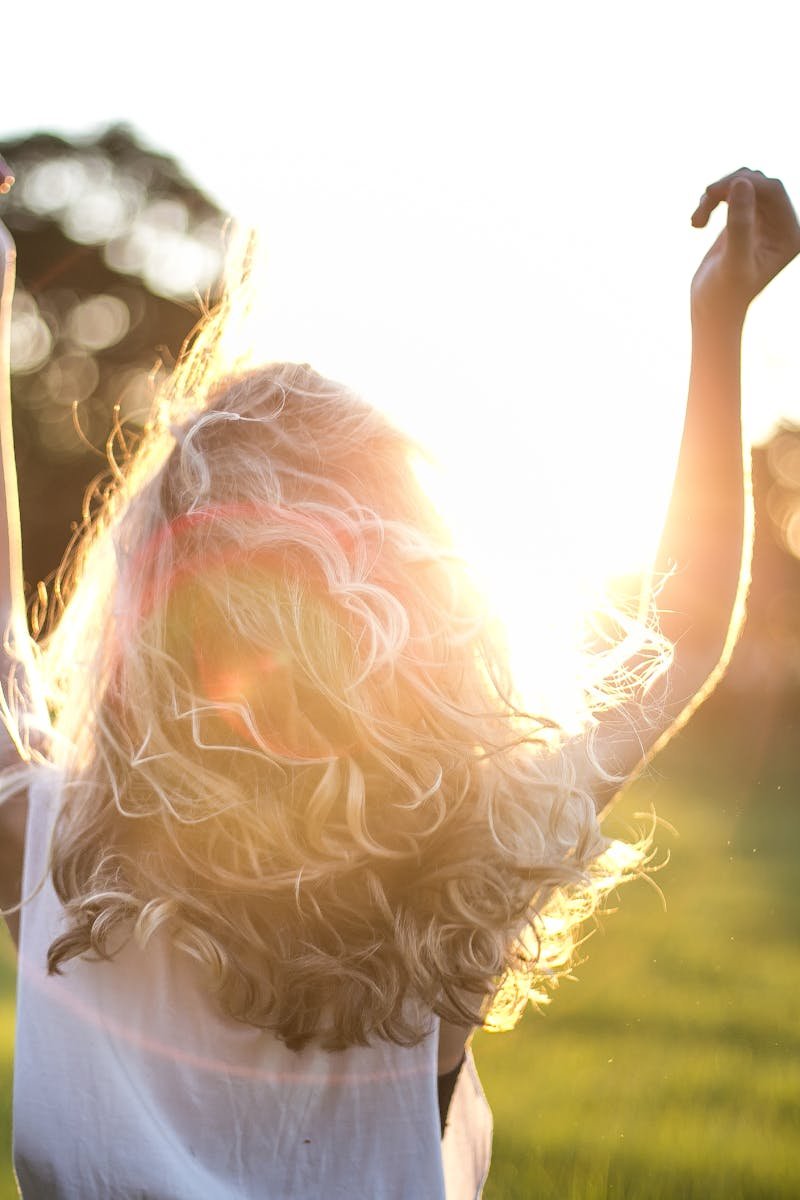 A woman with outstretched arms celebrates the sunset in a grassy field, capturing the essence of freedom and joy.