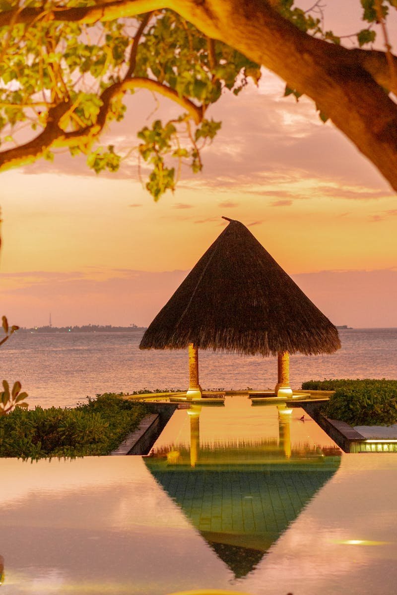 A tranquil scene of a tropical bungalow reflected in an infinity pool at sunset, evoking relaxation and luxury.