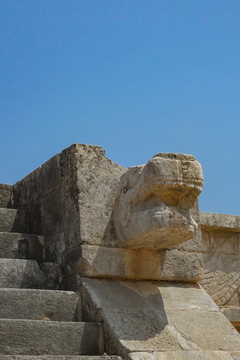 Close-up of the stone steps and serpent head sculpture at Chichen Itza under a clear blue sky.