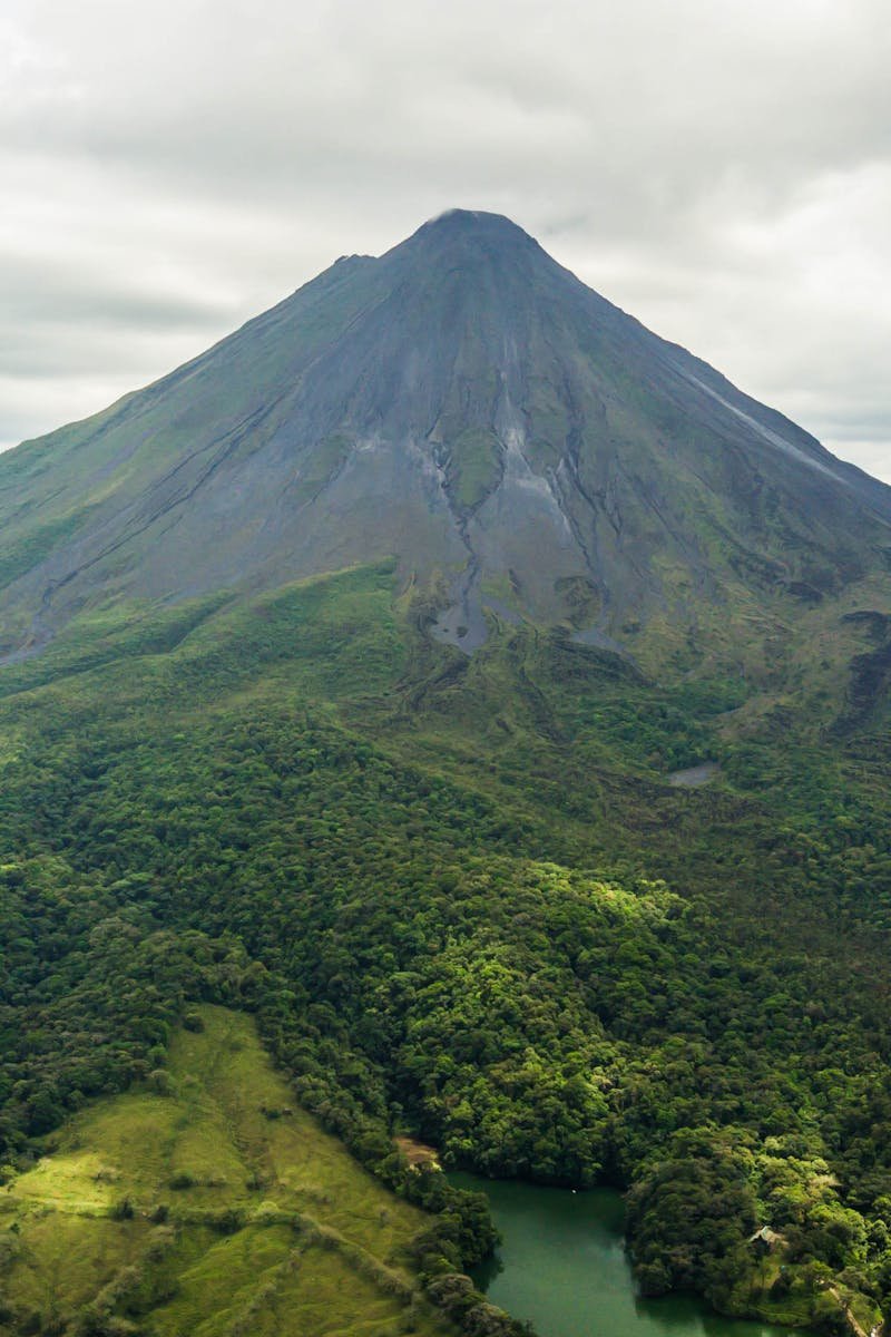 Dramatic aerial view of the lush green Arenal Volcano in Costa Rica against a cloudy sky.