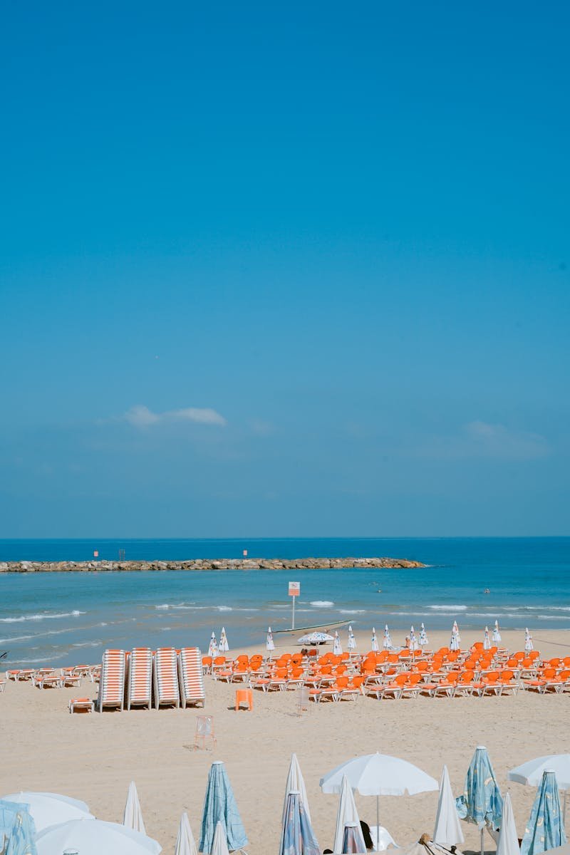 Sunny day at a vibrant beach in Tel Aviv, featuring orange sun loungers and umbrellas.