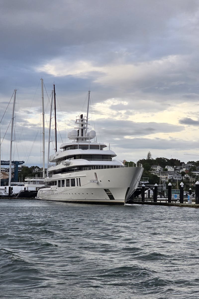 A majestic white yacht is docked at a marina under a cloudy sky, conveying luxury and serenity.