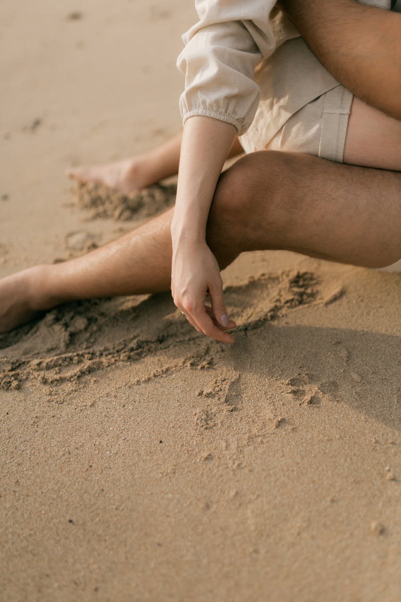 Couple sitting on sandy beach with entwined arms, capturing a moment of intimacy and relaxation.
