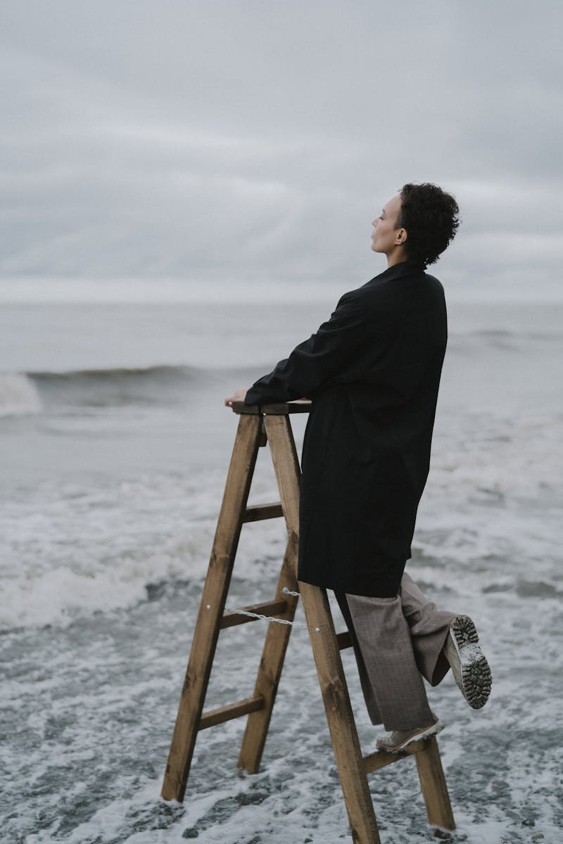 Woman standing on a ladder gazing at the ocean on an overcast day.