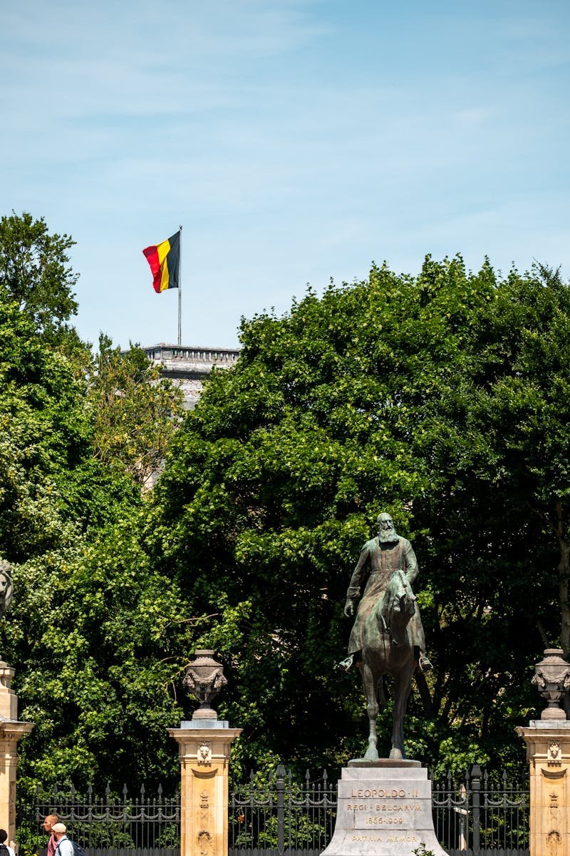 Equestrian statue and Belgian flag in a lush park setting in Brussels.