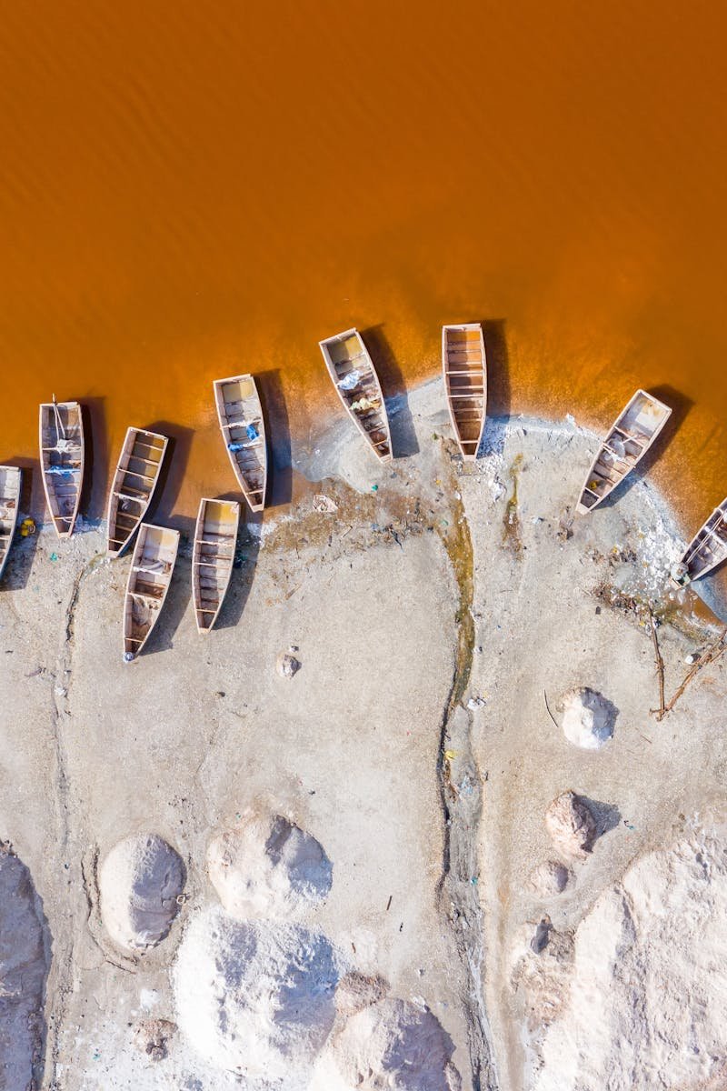 Drone view of small boats moored on white sandy shore of yellow muddy river