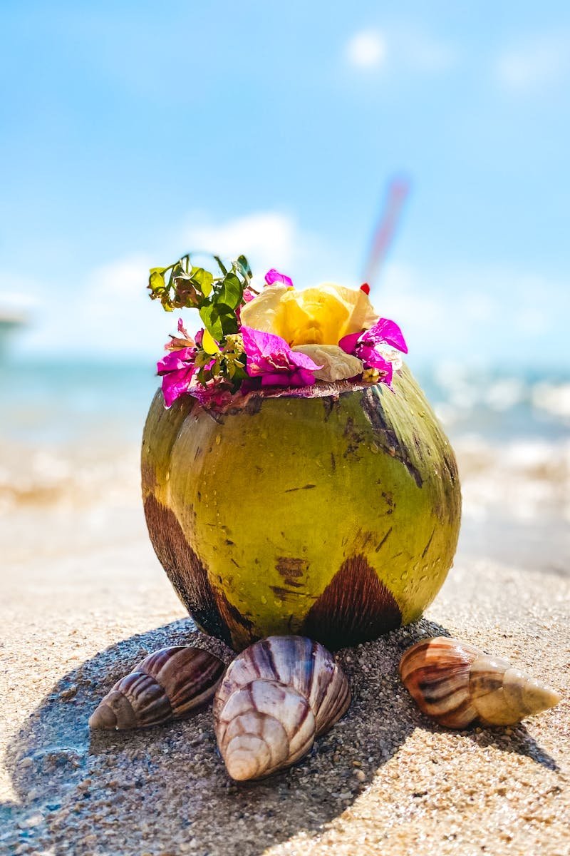 Vibrant coconut drink with flowers on sandy beach in Mauritius, ideal for tropical themes.